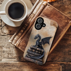 Könnte beinhalten: Eine Handyhülle mit einem schwarzen Drachen, der auf Büchern sitzt. Die Hülle hat einen Vintage-Papierhintergrund und einen Kameraausschnitt. Der Drache hat detaillierte Flügel und Schuppen. Die Hülle liegt auf einer Holzoberfläche neben einer Tasse Kaffee und einem Buch.
