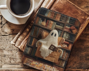 May include: A Halloween-themed mousepad featuring a ghost reading a book in a cozy armchair, set against a backdrop of a library. The mousepad has the name "Tabitha" printed on it. A cup of coffee and a book are also in the image.