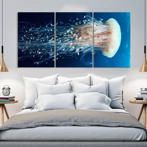 Op de afbeelding: Een driedelig canvasprint met een close-up van een kwal met lange, stromende tentakels tegen een blauwe achtergrond.