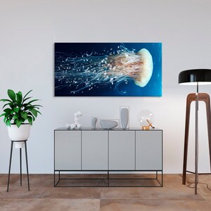 Op de afbeelding: Een grote, doorschijnende kwal met lange, zwevende tentakels drijft in een donkerblauwe oceaan. De kwal wordt verlicht door een helder licht, waardoor de ingewikkelde details worden benadrukt.