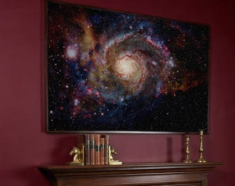 May include: A framed canvas print depicting a galaxy with swirling patterns in blue, red, and yellow hues. The artwork hangs above a wooden mantelpiece, adorned with brass candlesticks and bookends.