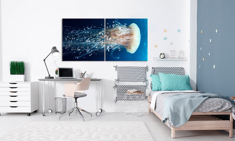Op de afbeelding: Een gesplitst wandkunstwerk op canvas met een close-up van een kwal met lange, stromende tentakels in een blauwe oceaan. Het kunstwerk wordt getoond in een slaapkamer met een bureau, een stoel en een bed met een blauw-wit gepatroneerd hoofdeinde.