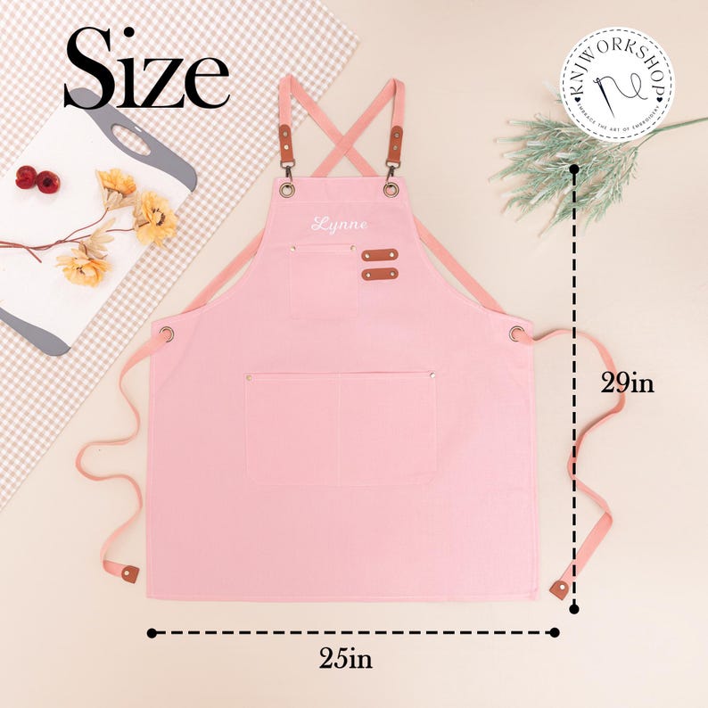May include: A pink apron with the name "Lynne" embroidered on the chest. The apron has two pockets and brown leather accents. It measures 29 inches in length and 25 inches in width.