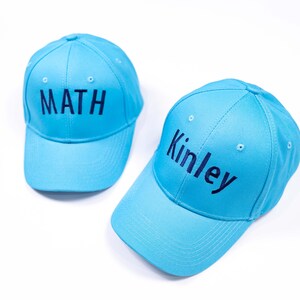 May include: Two blue baseball caps with embroidered text. One cap says "MATH" and the other says "Kinley".