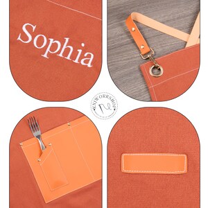 May include: An orange apron with the name "Sophia" embroidered in white. The apron has a leather strap and a pocket with a fork. The apron is designed for use in a kitchen or workshop.