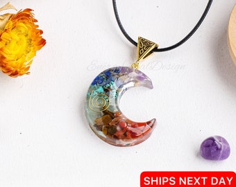 May include: A crescent moon pendant on a black cord necklace. The pendant is made of clear resin embedded with various colorful stones including red, brown, turquoise, and purple pieces, featuring a gold-toned metal spiral and a triangular bail.