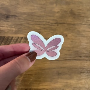 May include: A pink glitter butterfly sticker with a white outline.