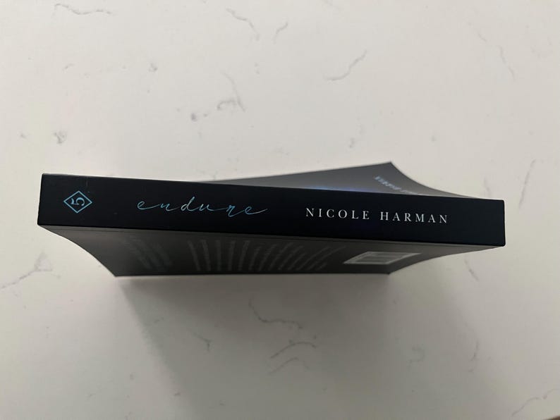 May include: A black book titled "endure" by Nicole Harman. The title is in a teal script font, and the author's name is in a white sans-serif font. The book has a teal diamond-shaped logo.