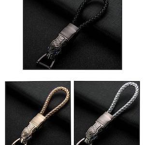 May include: Three keychains featuring a dragon design. The keychains are made of metal and have a braided leather loop. The dragon design is in black, gold, and silver.