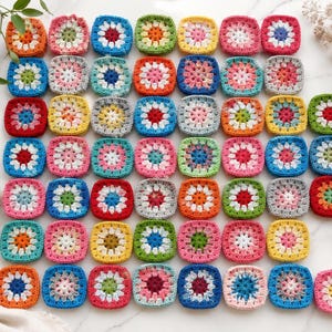 Peut inclure: Une collection de cinquante-sept motifs carrés au crochet disposés en grille. Chaque motif présente un dessin floral multicolore avec une couleur centrale entourée de nuances de fil contrastées, dont le rouge, bleu, jaune, rose, vert et orange.