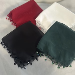 May include: Four square handkerchiefs in red, white, black, and green. Each handkerchief has a beaded trim along the edges. The handkerchiefs are made of a sheer fabric.