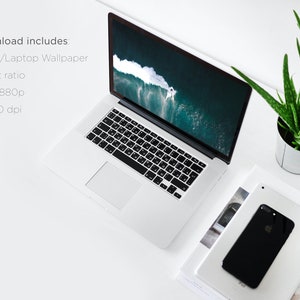 Puede incluir: Un ordenador port&aacute;til blanco con un teclado negro y una pantalla que muestra una foto de una ola rompiendo en el oc&eacute;ano. El port&aacute;til est&aacute; sobre una superficie blanca con una pila de revistas y una planta de aloe vera en maceta.