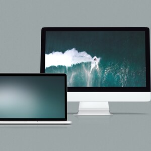 May include: A silver laptop computer with a dark blue screen and a silver desktop computer with a screen displaying an aerial view of a wave crashing in the ocean.