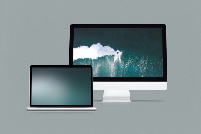 May include: A silver laptop computer with a dark blue screen and a silver desktop computer with a screen displaying an aerial view of a wave crashing in the ocean.