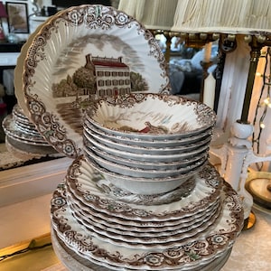 May include: A set of brown and white ceramic dinnerware with a floral pattern and a pheasant design. The set includes a large dinner plate, a smaller plate, and a bowl.