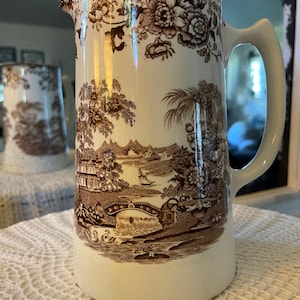 May include: A white ceramic mug with a black handle and the text "But First, Coffee" in a black, bold font. The mug is on a white surface.