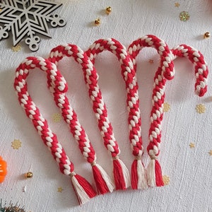 Könnte beinhalten: Fünf rote und weiße Zuckerstangen-Ornamente mit weißen Quasten. Die Ornamente sind in einer Reihe auf einer weißen Oberfläche angeordnet.