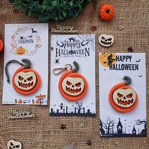 May include: Three Halloween-themed keychains featuring orange and brown yarn pumpkins with carved faces. Each keychain is attached to a card with a Halloween-themed design and the text "Happy Halloween".