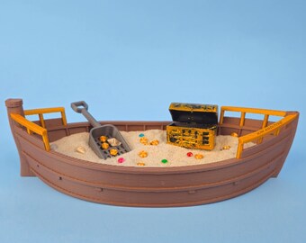 May include: A brown wooden toy boat filled with sand, gold coins, and a small gold treasure chest. A miniature shovel is resting on the sand.