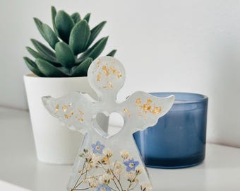 May include: White resin angel figurine with gold leaf accents and a heart-shaped cutout. The angel is decorated with pressed blue and white flowers.