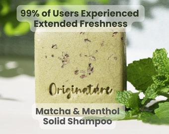 May include: A green bar of soap with the words "Originature Matcha & Menthol Solid Shampoo" printed on the front. The soap is sitting on a white surface next to a sprig of green mint.
