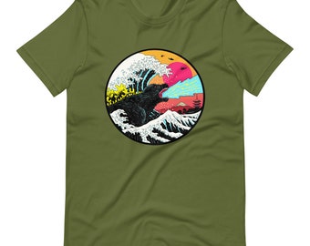 May include: A green t-shirt with a graphic print of a monster roaring in front of a large wave. The wave is in a circle with a red sun and a yellow sky in the background.