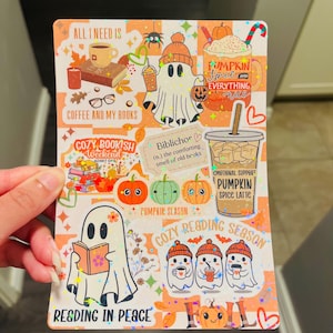 May include: A colorful sticker sheet with fall-themed illustrations. It features ghost characters, pumpkins, coffee cups, and text like "Pumpkin Spice Latte" and "Cozy Reading Season." The overall design has a warm, inviting aesthetic.