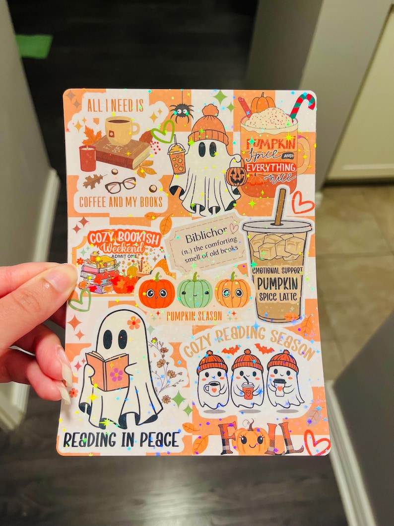 May include: A colorful sticker sheet with fall-themed illustrations. It features ghost characters, pumpkins, coffee cups, and text like "Pumpkin Spice Latte" and "Cozy Reading Season." The overall design has a warm, inviting aesthetic.