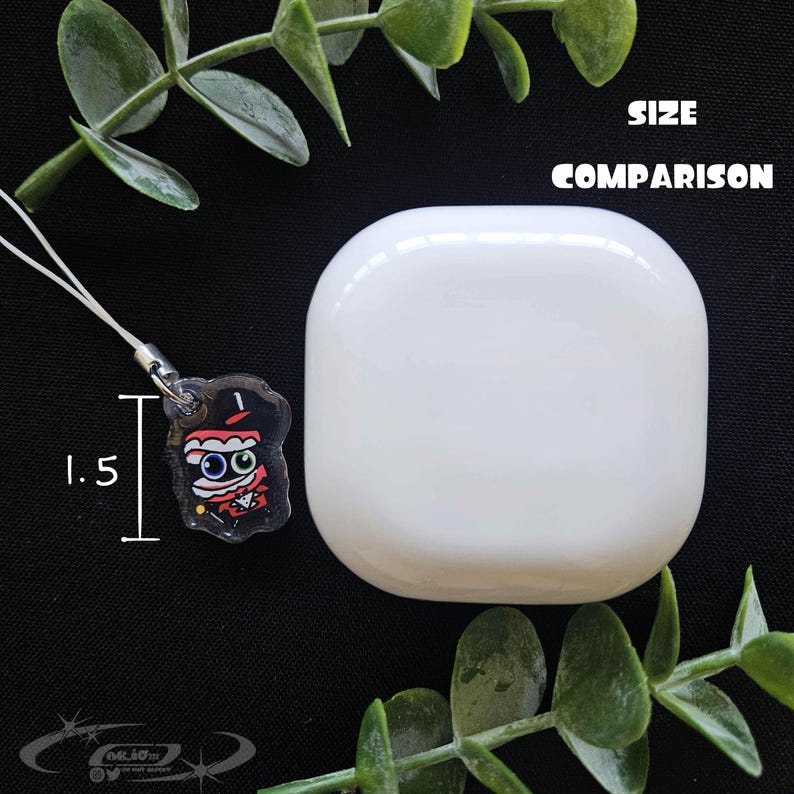 May include: A white, rounded square object next to a small, clear charm with a cartoon character design. The charm is 1.5 inches in height. The text "SIZE COMPARISON" is above the white object.