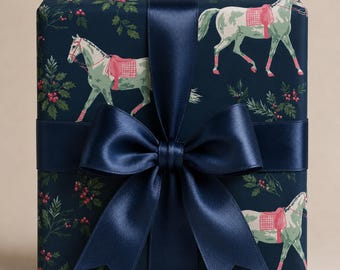 Puede incluir: Una caja de regalo rectangular envuelta en papel azul marino oscuro con un patrón repetitivo de caballos verde claro con sillas de montar a cuadros rojos y ramas de acebo verdes con bayas rojas, atada con un lazo de satén azul marino.