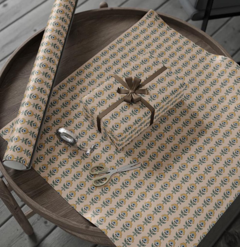 May include: Gift wrapping paper with a repeating floral pattern in yellow, blue, and green on a beige background. A wrapped gift with a brown ribbon and bow sits on the paper. A roll of paper, scissors, and tape are also visible.