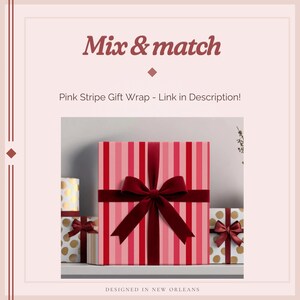 K&ouml;nnte beinhalten: Ein quadratisches Geschenkpaket in rosa-rot gestreiftem Papier, verziert mit einer dunkelroten Samtschleife. Flankiert wird das Paket von kleineren Geschenken mit goldenen Punkten, die ebenfalls mit dunkelroten Samtschleifen versehen sind.