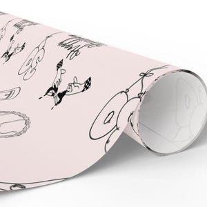 K&ouml;nnte beinhalten: Eine Rolle hellrosa Geschenkpapier mit einem sich wiederholenden schwarzen Strichzeichnungsmuster aus Luftballons, Partyh&uuml;ten und dem Text "Be Happy". Das Papier ist in einer zylindrischen Rollenform dargestellt und zeigt das Design.