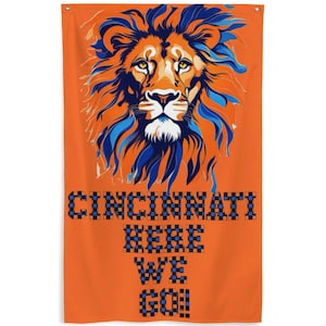 May include: Orange flag with a blue and orange lion head illustration. The text "CINCINNATI HERE WE GO!" is in a checkered pattern with blue and orange squares.