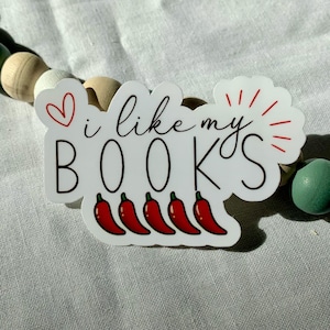 May include: White sticker with the text "i like my BOOKS" in black cursive font. A red heart is above the text and a red sunburst is to the right. Five red chili peppers are below the text.