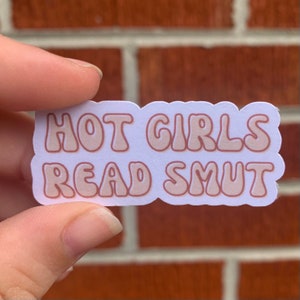 May include: A white sticker with rounded edges features the text "HOT GIRLS READ SMUT" in a light brown color with a bubble-like font.