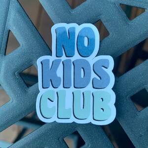 May include: A blue, green, and white sticker with the text "NO KIDS CLUB" in a stylized font.