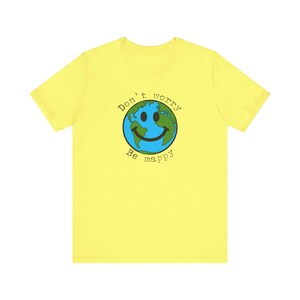 以下が含まれることがあります： 黄色のTシャツに、緑と青の地球のグラフィックと「Don't worry Be mappy」の文字がプリントされています。