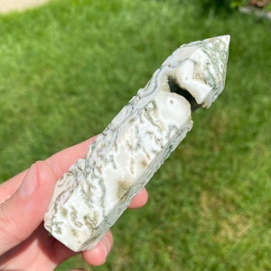 May include: A white and green agate crystal point with a unique, natural, and organic pattern. The crystal is polished and has a smooth, glassy surface.
