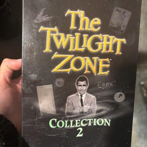 May include: A black DVD box with a green and white title "The Twilight Zone Collection 2". The box features a black and white image of Rod Serling, the show's creator, against a dark background with various images and text.