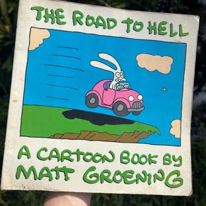 May include: A cartoon book cover with a pink car driven by a white rabbit with a blue sky and green grass in the background. The title of the book is "The Road to Hell" and the author is "Matt Groening".