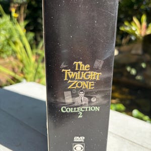 May include: A black DVD box with a gold title that reads "The Twilight Zone Collection 2". The box features a black and white image of Rod Serling, the creator of the show, and a CBS DVD logo.