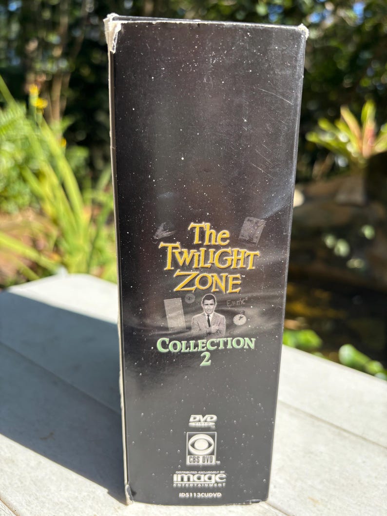 May include: A black DVD box with a gold title that reads "The Twilight Zone Collection 2". The box features a black and white image of Rod Serling, the creator of the show, and a CBS DVD logo.