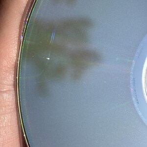 May include: Close-up of a silver-colored CD with a rainbow-colored ring around the edge. The CD has a few scratches on the surface.