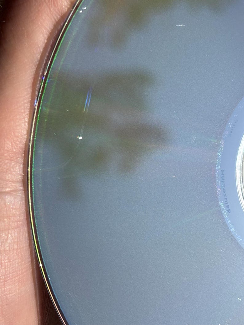 May include: Close-up of a silver-colored CD with a rainbow-colored ring around the edge. The CD has a few scratches on the surface.