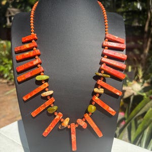 May include: A necklace made of orange and green stones. The stones are in the shape of long rectangles and are strung on a thin orange cord.