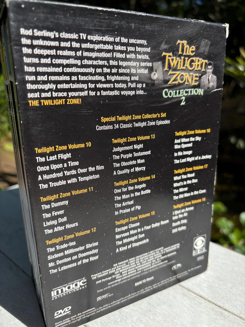 May include: A black DVD box set with a silver title, "The Twilight Zone Collection 2". The box features a photo of Rod Serling, the creator of the show, and a list of episodes included in the set.