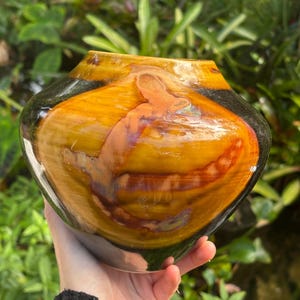 May include: A ceramic vase with a rounded, bulbous shape. The vase is glazed in a dark brown color with streaks of orange, yellow, and red. The glaze has a glossy finish.