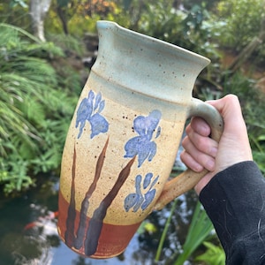 May include: A ceramic pitcher with a light blue, brown, and orange glaze. The pitcher has a handle and is decorated with a floral design.