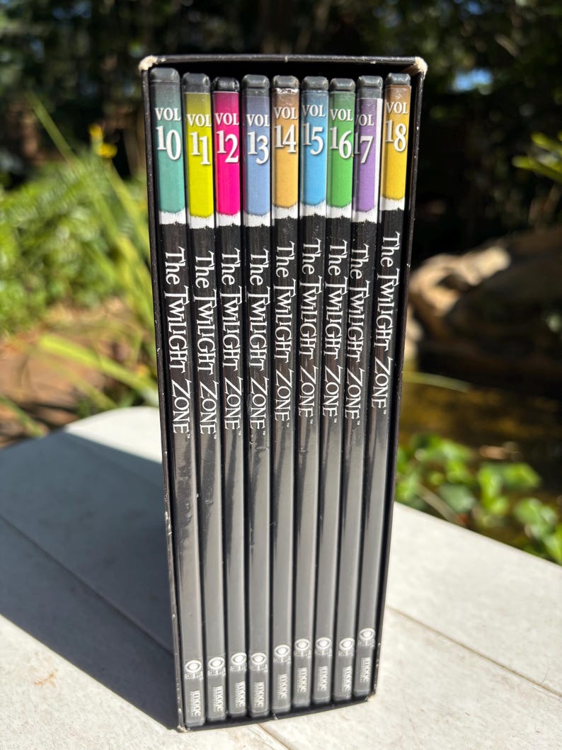 May include: A set of eight DVD cases for The Twilight Zone, volumes 10 through 18. The cases are black with a silver spine and feature a colorful design with the volume number and show title.